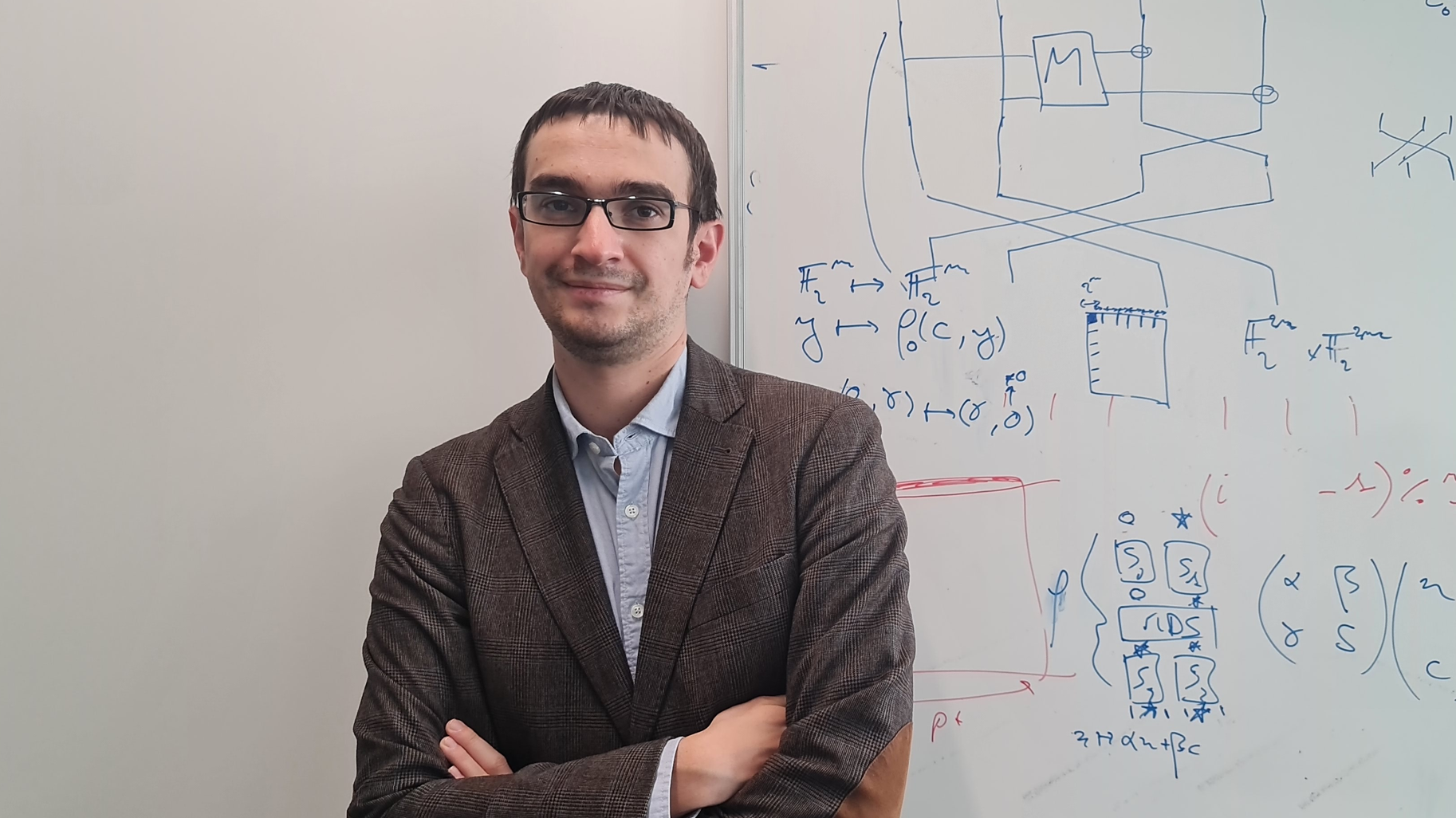 Portrait de Léo Perrin devant un tableau blanc rempli de formules scientifiques