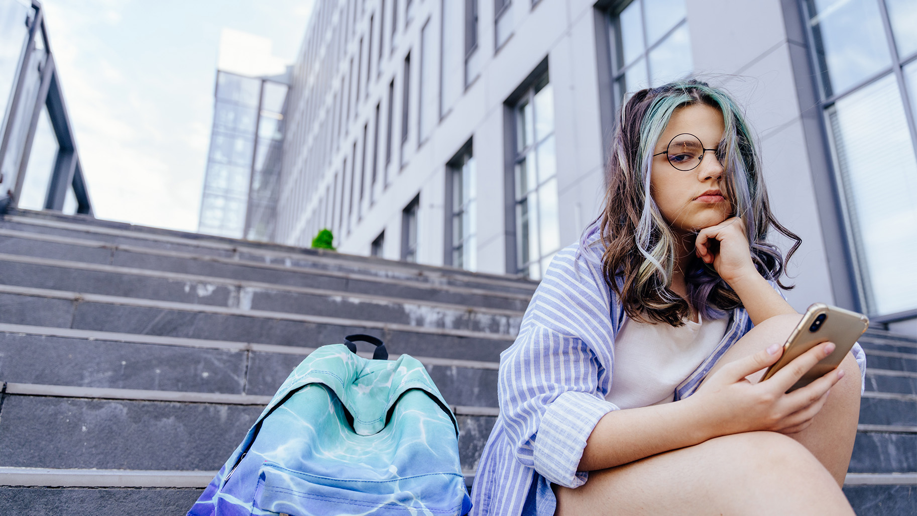 Jeune élève triste sur des escaliers avec un smartphone à la main